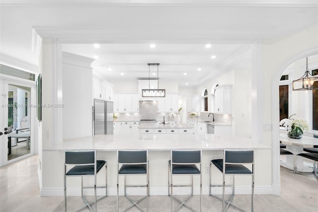 kitchen with white cabinetry, hanging light fixtures, built in fridge, decorative backsplash, and a breakfast bar