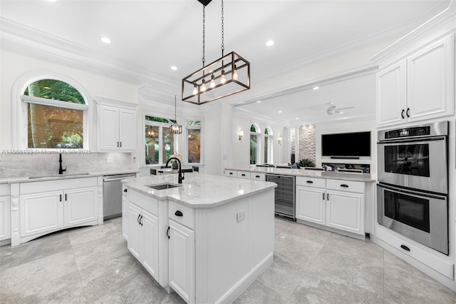 kitchen featuring stainless steel appliances, beverage cooler, sink, white cabinets, and an island with sink