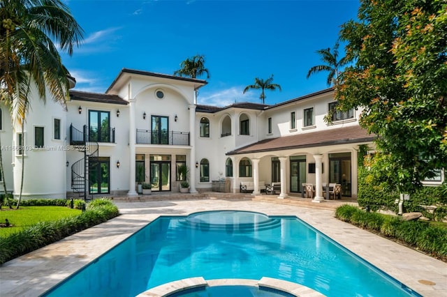 back of house with a swimming pool with hot tub, a balcony, and a patio