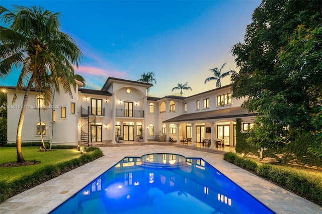 back house at dusk with a patio area, a balcony, and a pool with hot tub