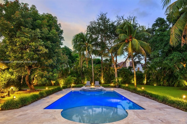 pool at dusk with a patio area and an in ground hot tub