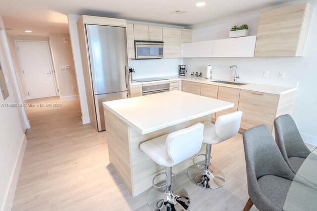 kitchen with a breakfast bar, light hardwood / wood-style floors, sink, a kitchen island, and stainless steel appliances