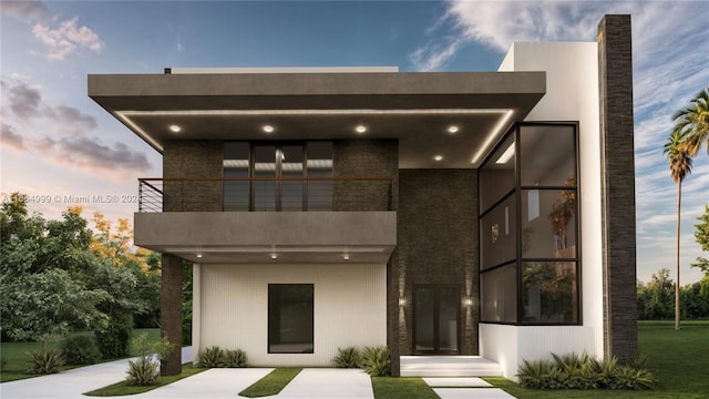 back house at dusk with a balcony and a yard