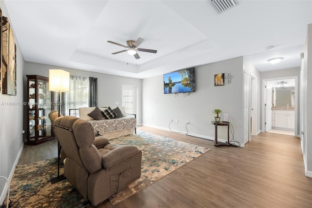 living room featuring wood-type flooring, ceiling fan, and a tray ceiling