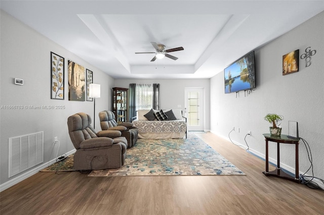 living room with wood-type flooring, a raised ceiling, and ceiling fan