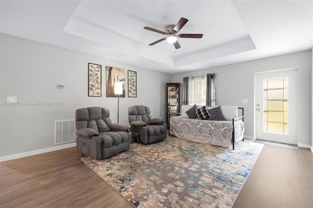 living room featuring ceiling fan, wood-type flooring, and a raised ceiling