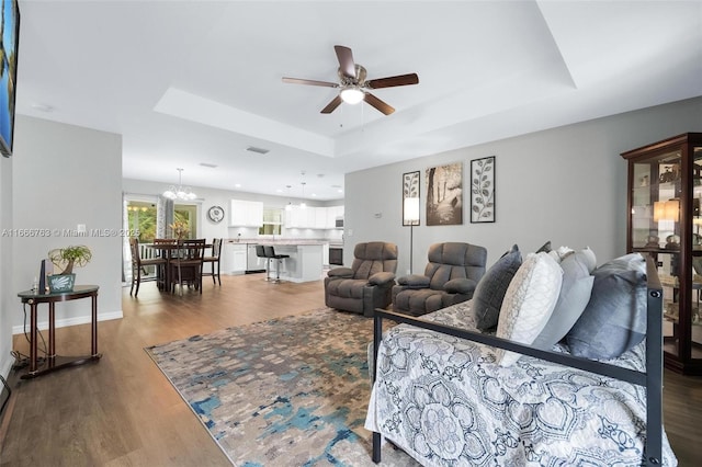 living room with a raised ceiling, wood-type flooring, and ceiling fan with notable chandelier