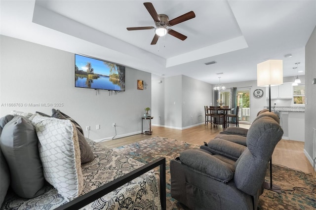 living room featuring a raised ceiling, ceiling fan with notable chandelier, and light hardwood / wood-style floors