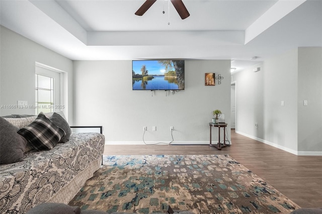 living room featuring hardwood / wood-style floors, ceiling fan, and a tray ceiling