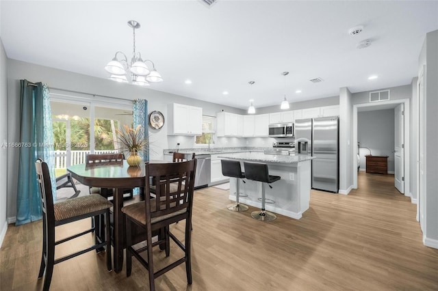 dining area with sink, light hardwood / wood-style floors, and a notable chandelier