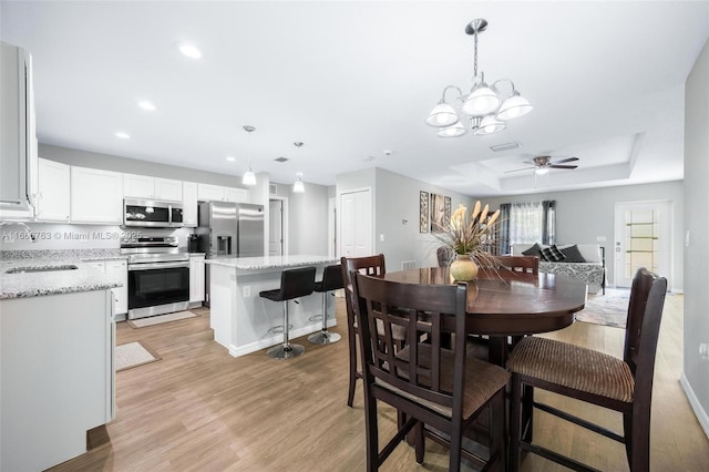 dining room with sink, a raised ceiling, ceiling fan, and light wood-type flooring