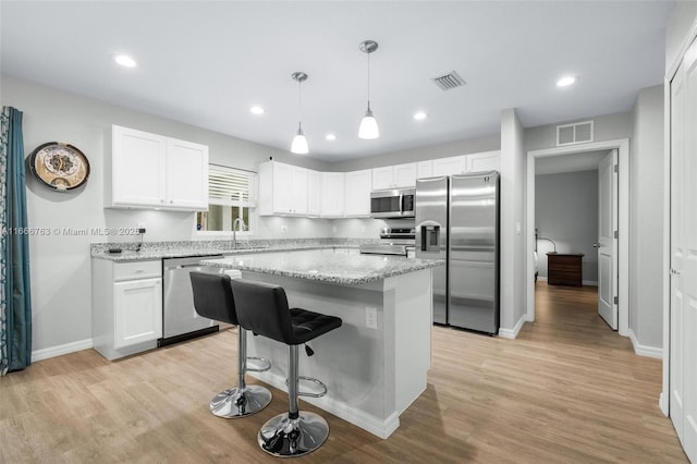 kitchen with appliances with stainless steel finishes, sink, white cabinets, a center island, and light stone counters