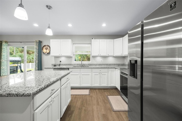 kitchen with appliances with stainless steel finishes, white cabinets, hanging light fixtures, light stone counters, and a healthy amount of sunlight