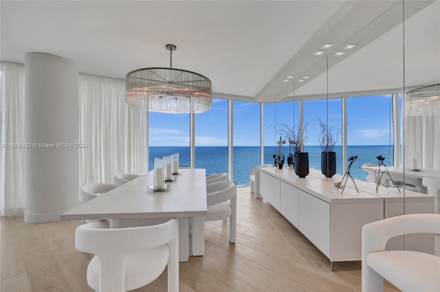 dining room featuring floor to ceiling windows, a notable chandelier, light wood-style floors, and a water view