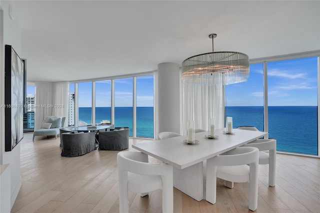 dining space featuring a water view, light wood-type flooring, an inviting chandelier, and floor to ceiling windows