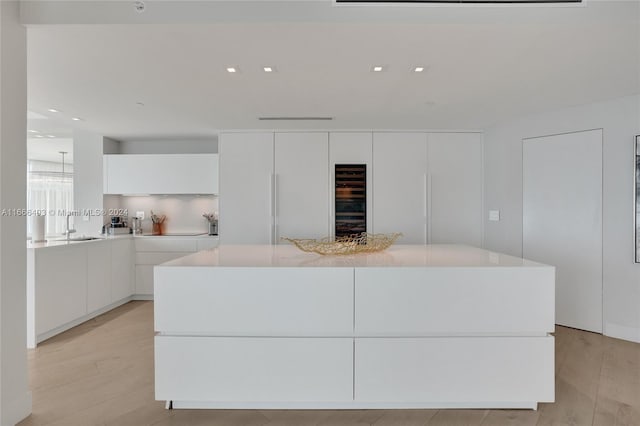 kitchen with modern cabinets, light wood-type flooring, white cabinets, a center island, and light countertops