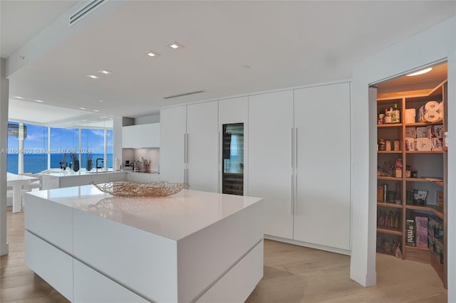 kitchen with a water view, white cabinetry, a center island, light hardwood / wood-style flooring, and sink