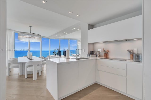 kitchen featuring sink, white cabinets, a water view, decorative light fixtures, and black electric cooktop