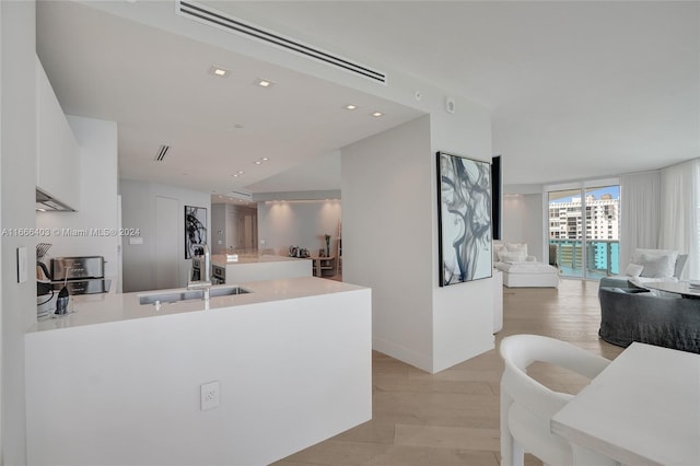 kitchen with sink, a wall of windows, light hardwood / wood-style floors, and white cabinetry