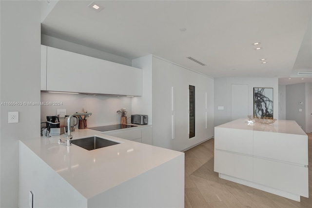 kitchen with light hardwood / wood-style flooring, white cabinetry, a kitchen island, and sink