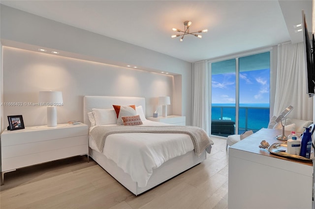 bedroom featuring an inviting chandelier, a water view, light wood-style floors, access to outside, and expansive windows