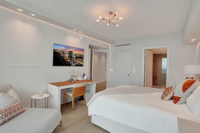 bedroom with a notable chandelier, light wood-type flooring, and ensuite bathroom