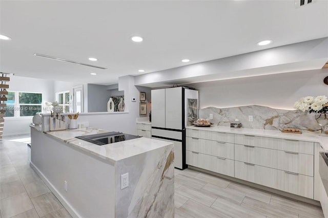 kitchen with light stone counters, white refrigerator, a kitchen island, backsplash, and black electric cooktop