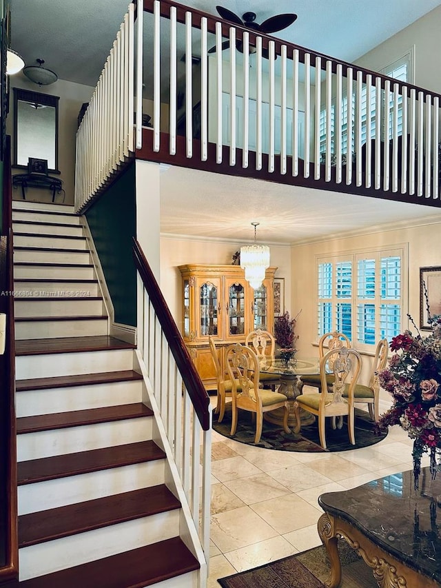 stairway featuring ceiling fan with notable chandelier, tile patterned flooring, and crown molding