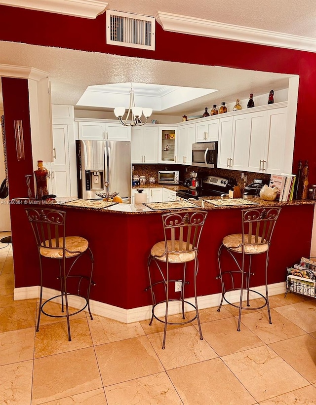 kitchen with a notable chandelier, white cabinetry, kitchen peninsula, stainless steel appliances, and crown molding