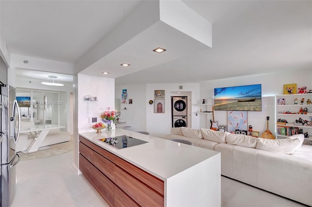 kitchen featuring black electric stovetop, stainless steel fridge, a kitchen island, and stacked washer and dryer