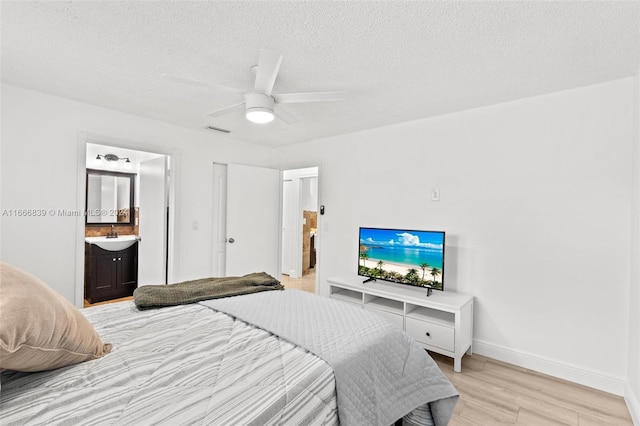 bedroom featuring a textured ceiling, sink, light hardwood / wood-style flooring, ensuite bathroom, and ceiling fan