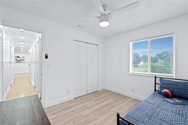 bedroom featuring a textured ceiling, light hardwood / wood-style floors, ceiling fan, and a closet