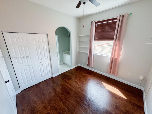 unfurnished bedroom with ceiling fan, ensuite bathroom, wood-type flooring, and a closet