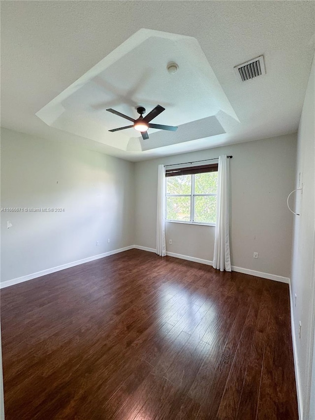 spare room featuring dark wood-type flooring, ceiling fan, a textured ceiling, and a tray ceiling