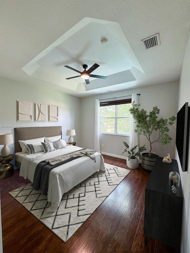 bedroom featuring hardwood / wood-style flooring, a textured ceiling, ceiling fan, and a raised ceiling