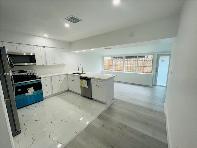 kitchen with white cabinets, sink, kitchen peninsula, stainless steel appliances, and light hardwood / wood-style floors