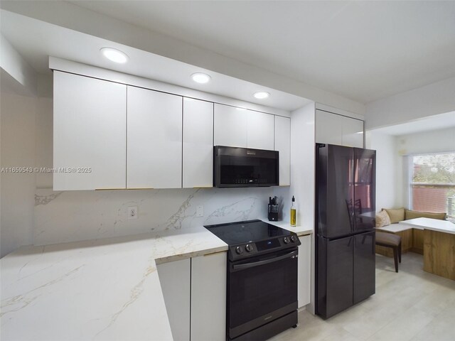 kitchen with light stone countertops, backsplash, white cabinetry, and black appliances