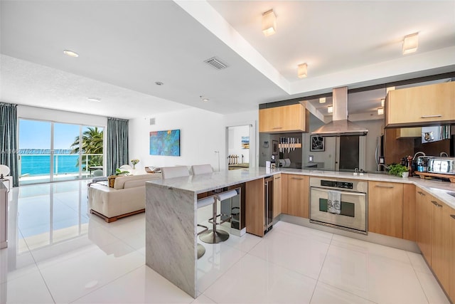 kitchen featuring kitchen peninsula, island range hood, a water view, oven, and light stone countertops