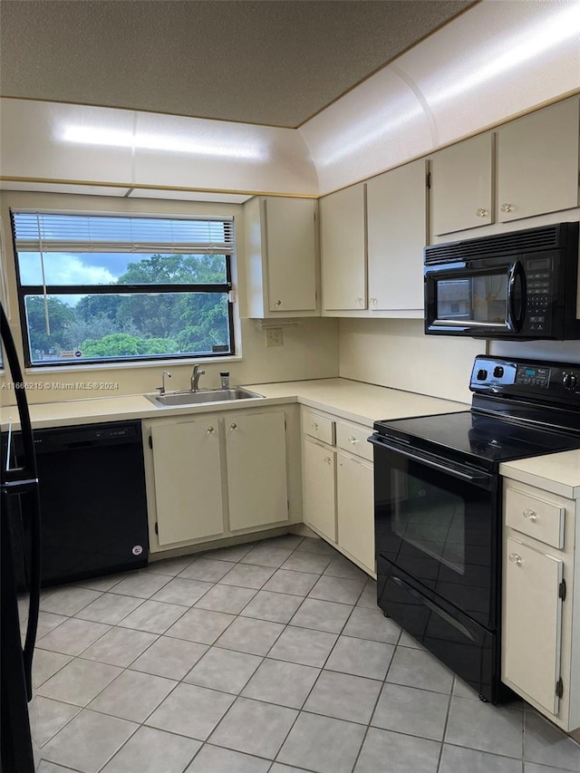 kitchen featuring light tile patterned floors, cream cabinets, sink, and black appliances