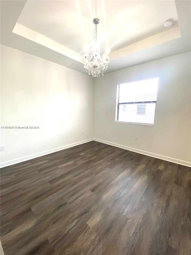 unfurnished room featuring a tray ceiling, dark wood-type flooring, and a chandelier