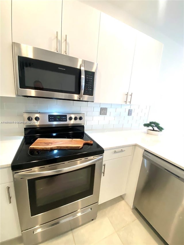 kitchen with appliances with stainless steel finishes, backsplash, light tile patterned floors, and white cabinetry