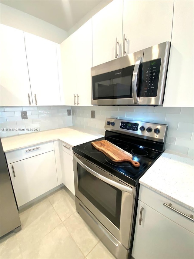 kitchen featuring light tile patterned flooring, stainless steel appliances, backsplash, and white cabinetry