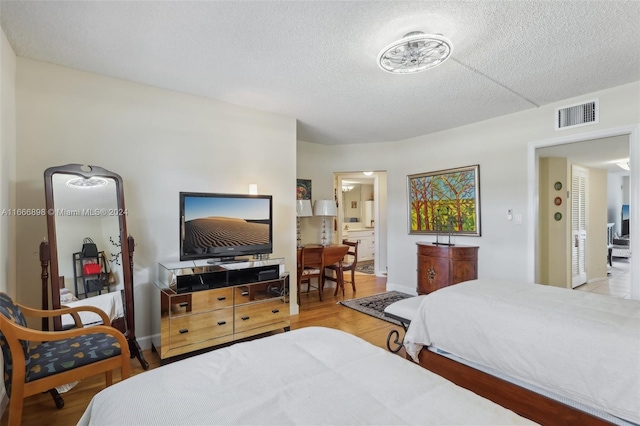 bedroom with ensuite bathroom, a textured ceiling, and light wood-type flooring