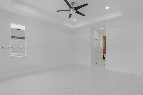 empty room featuring a tray ceiling and ceiling fan