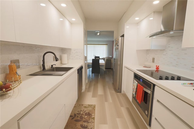 kitchen with sink, tasteful backsplash, wall chimney range hood, white cabinetry, and stainless steel appliances