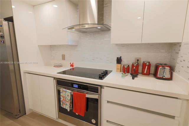 kitchen featuring white cabinets, wall chimney exhaust hood, stainless steel appliances, light hardwood / wood-style flooring, and backsplash