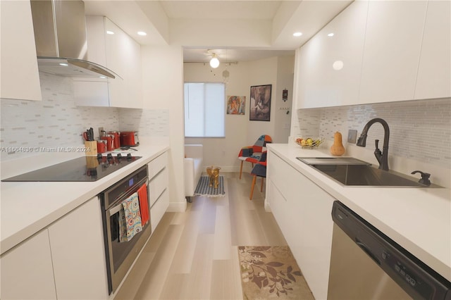 kitchen with appliances with stainless steel finishes, white cabinetry, tasteful backsplash, sink, and wall chimney range hood