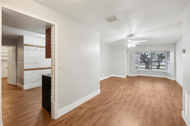 unfurnished room with ceiling fan, light wood-type flooring, and brick wall