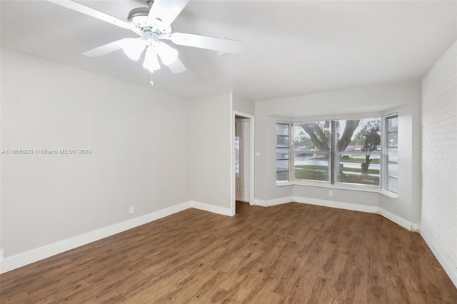 spare room featuring dark hardwood / wood-style floors, ceiling fan, and brick wall