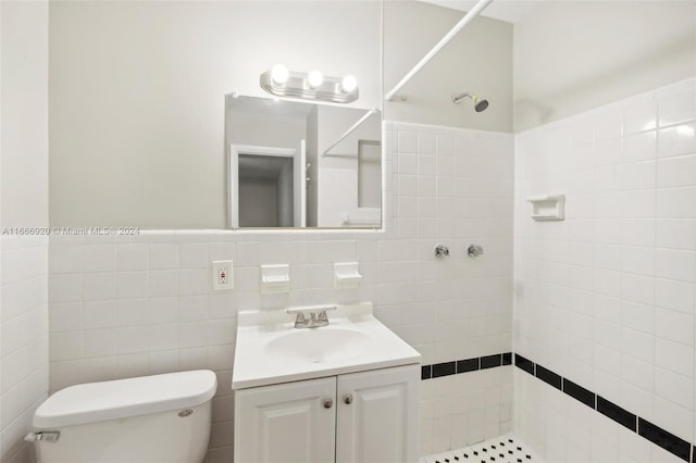 bathroom with tile walls, tiled shower, vanity, and toilet